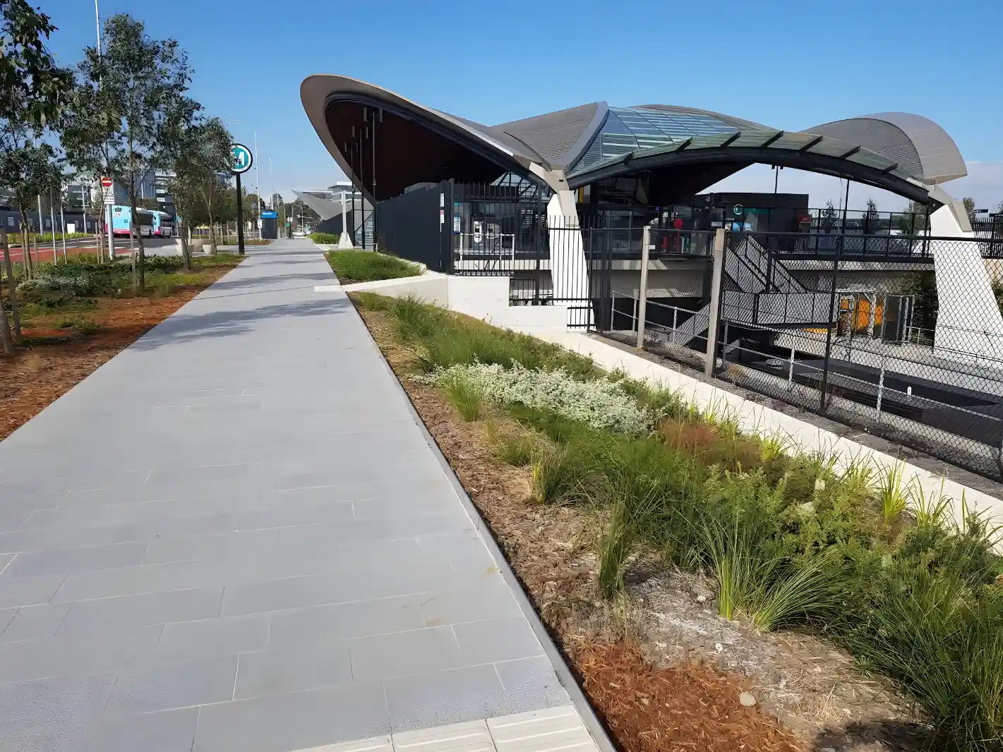 A modern pedestrian walkway alongside Bella Vista railway station with landscaped areas and a clear blue sky