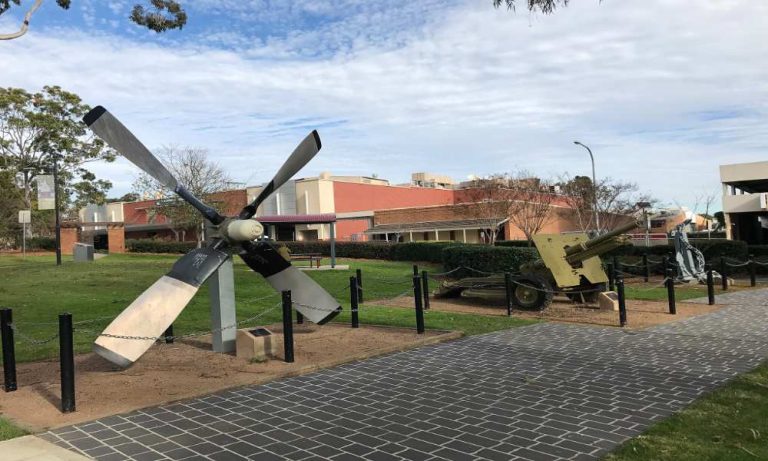 Outdoor display of historical military artifacts including a large aircraft propeller and artillery pieces at Mawson Park, Campbelltown, New South Wales.