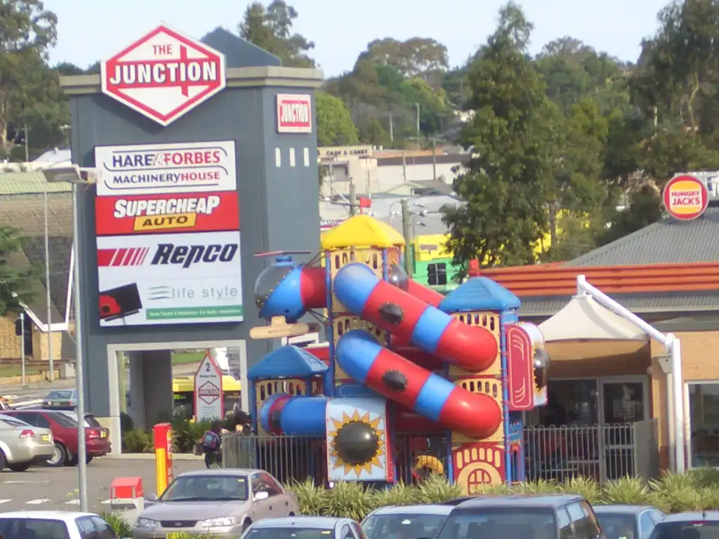 Large inflatable play structure with bright colors in front of a commercial area with various store signs, including 'The Junction in northmead